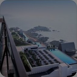 아난티 앳 부산 코브 — 어두운 발코니 난간 너머로 내려다본 아난티 코브 리조트의 루프탑 풀, 선베드 데크와 바위 해안