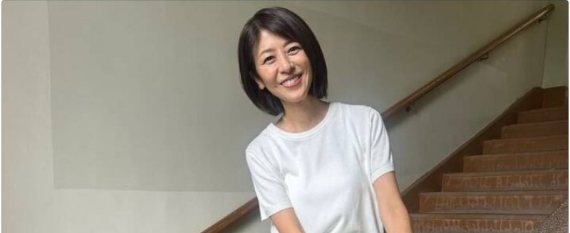 白いTシャツを着てショートボブの女性が階段の手すりの前で微笑んでいる