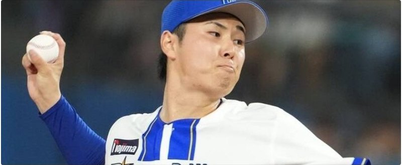 青い帽子と白いユニフォーム姿の野球投手が、ボールを持った手を上げて正面を見つめている